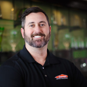SERVPRO Employee Smiling with a green background and black shirt with SERVPRO logo